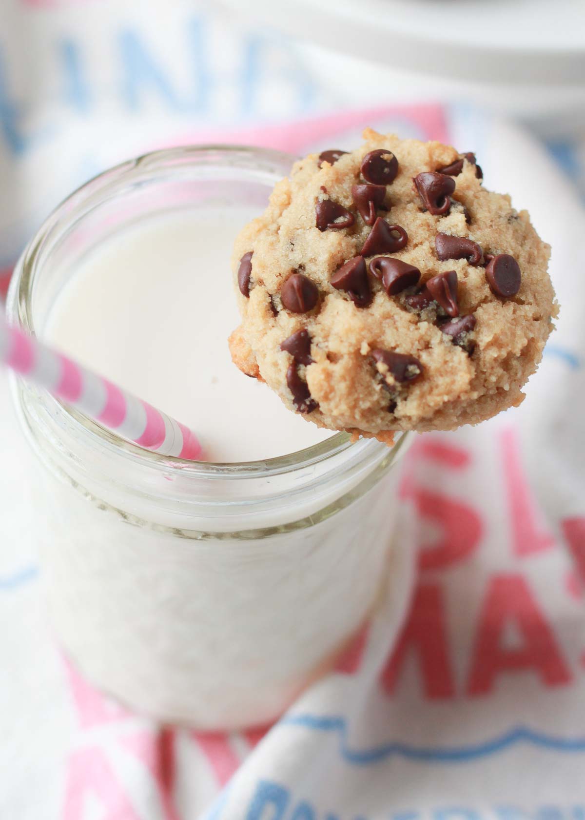 A single soft-baked almond milk chocolate chip cookie on the rim of a glass of almond milk. 