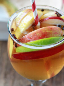 A clear glass full of apple cider sangria with a red and white straw