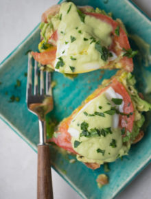 Two pieces of avocado eggs Benedict on a teal plate with a fork.