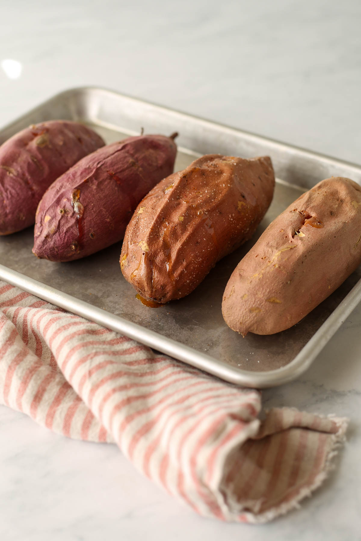Four baked sweet potatoes on a cookie sheet.