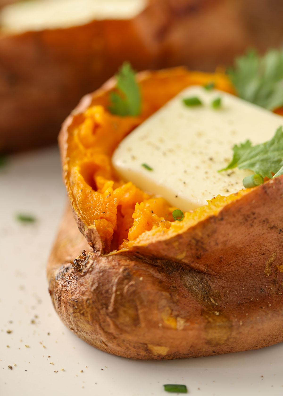 A close-up of a baked sweet potato with a pat of butter and fresh herbs.