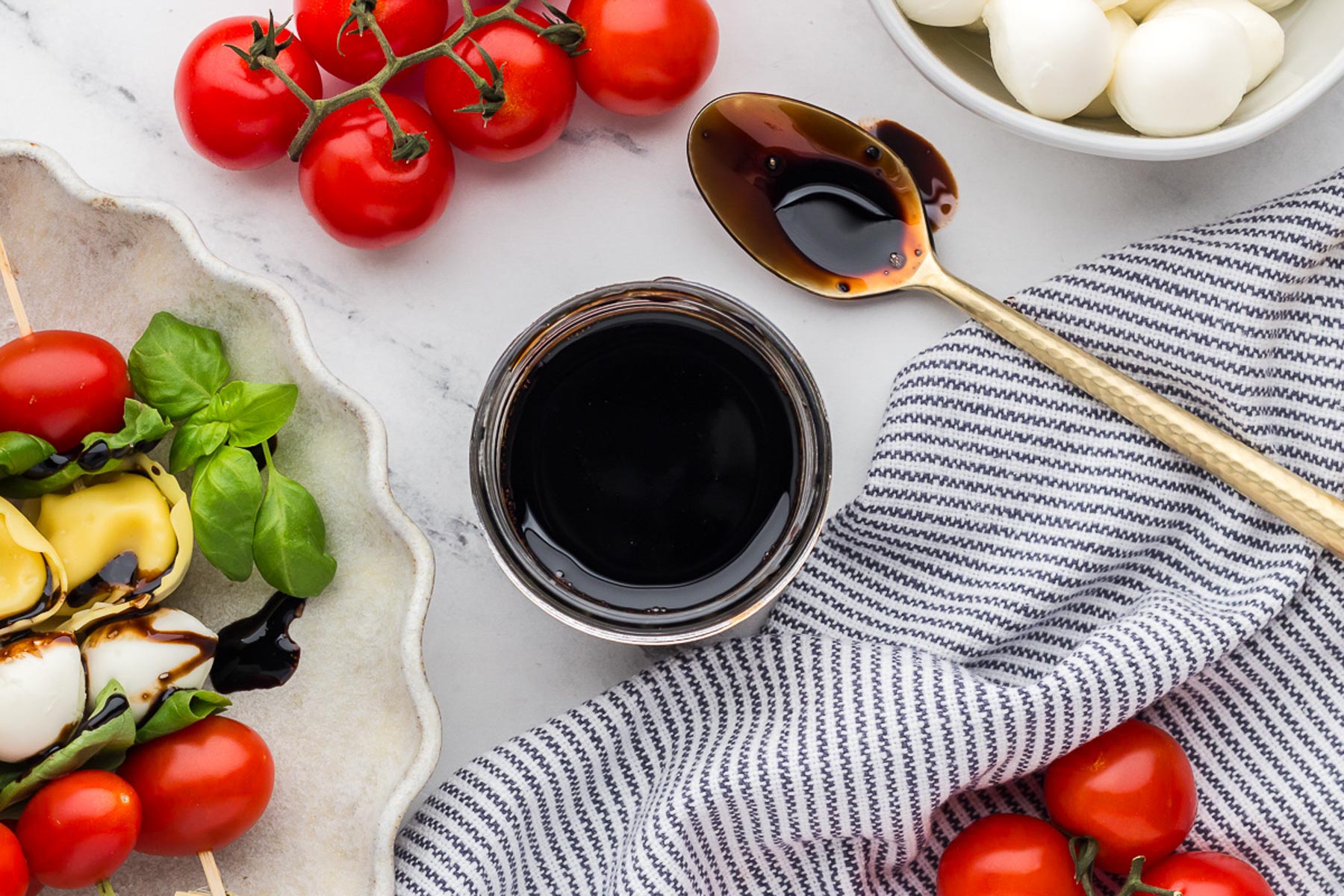 a jar of balsamic glaze with a spoon next to it and a striped napkin