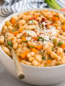 White bowl full of Vegetarian Navy Bean Soup with a gold spoon in it and a striped napkin in the background