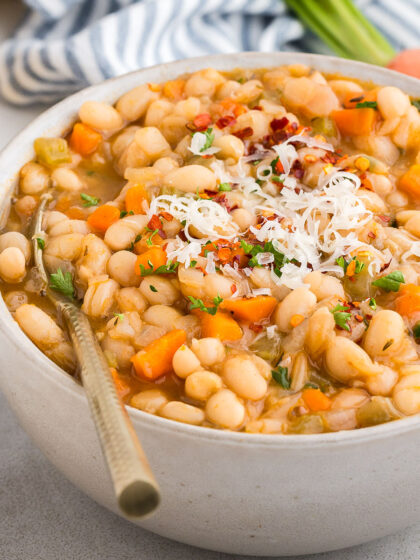 White bowl full of Vegetarian Navy Bean Soup with a gold spoon in it and a striped napkin in the background