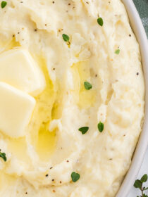 Close-up top view of Best Ever Mashed Potatoes with cream cheese in an oval dish with thyme leaves and a pat of butter.