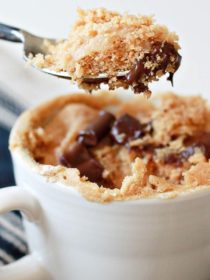 A spoon scoops out a spoonful of rich and decadent peanut butter mug cake with melted chocolate. A white teacup contains the mug cake.