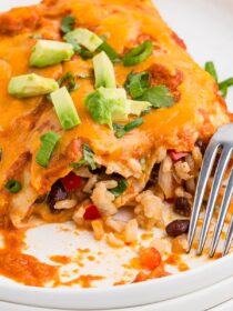 A stack of white plates with a serving of Black Bean & Rice Enchiladas and a silver fork