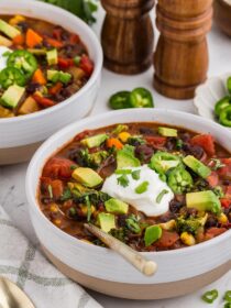 Two bowls of Black Bean Veggie Chili with a gold spoon and salt and pepper shakers in the background