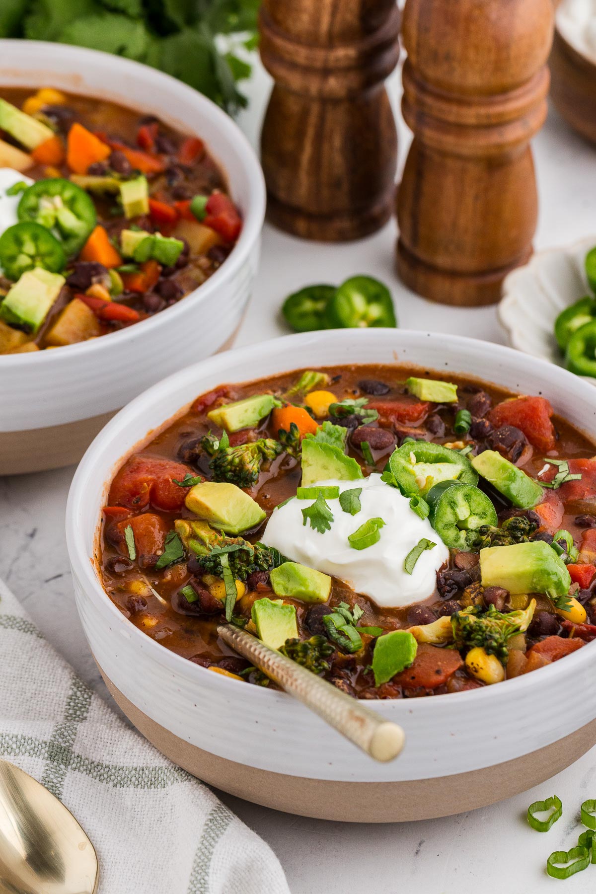 Two bowls of Black Bean Veggie Chili with a gold spoon and salt and pepper shakers in the background