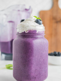 A blueberry milkshake with whipped cream, blueberries, and mint.