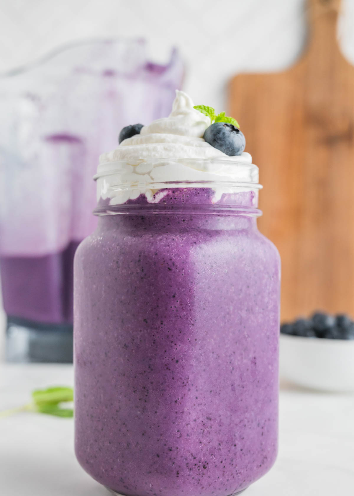 A blueberry milkshake with whipped cream, blueberries, and mint.