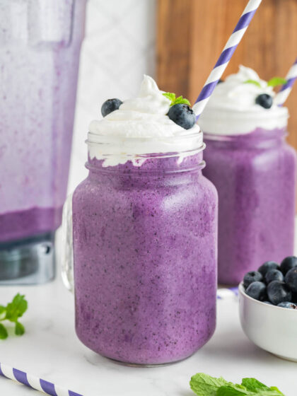 Two blueberry milkshakes with a blender in the background.