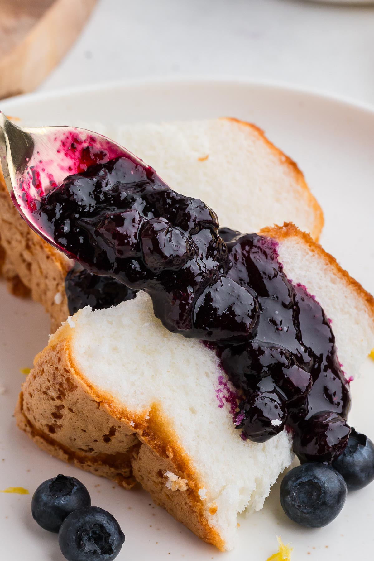 a spoon spooning blueberry sauce over two pieces of angel food cake
