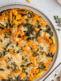 Top view of Butternut Squash & Spinach Pasta Bake on a platter with thyme and parmesan cheese in the background.