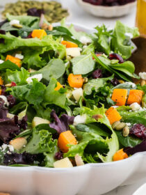 Roasted Butternut Squash Feta Salad in a white bowl with salad servers.