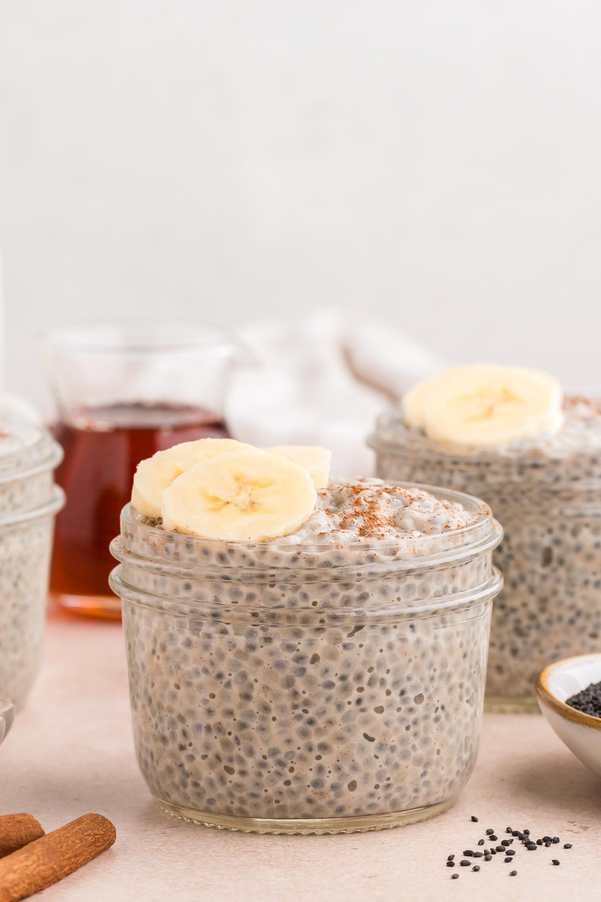 Chai Latte Basil Seed Pudding in small mason jars with cinnamon and sliced bananas.