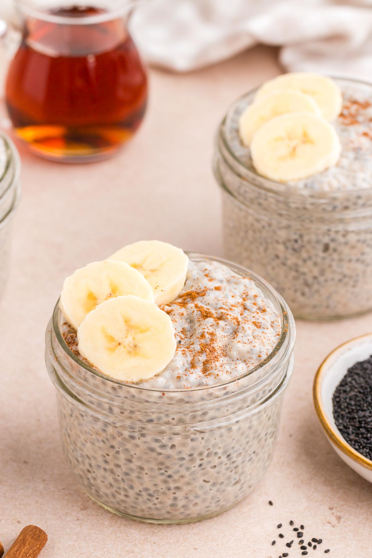 Chai Latte Basil Seed Pudding in small mason jars with cinnamon and sliced bananas