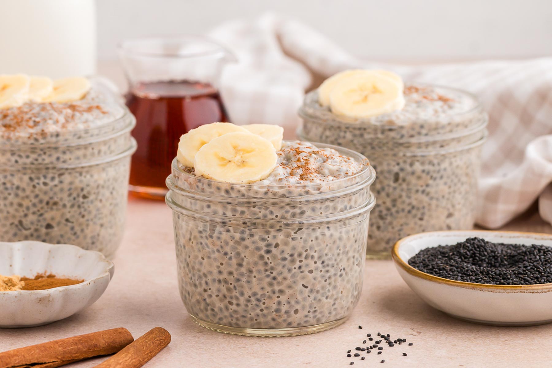 Chai Basil Seed Pudding in small mason jars with cinnamon and sliced bananas