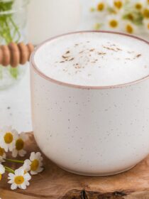 Stoneware mug full of Chamomile Latte on a wooden board and chamomile flowers in the background