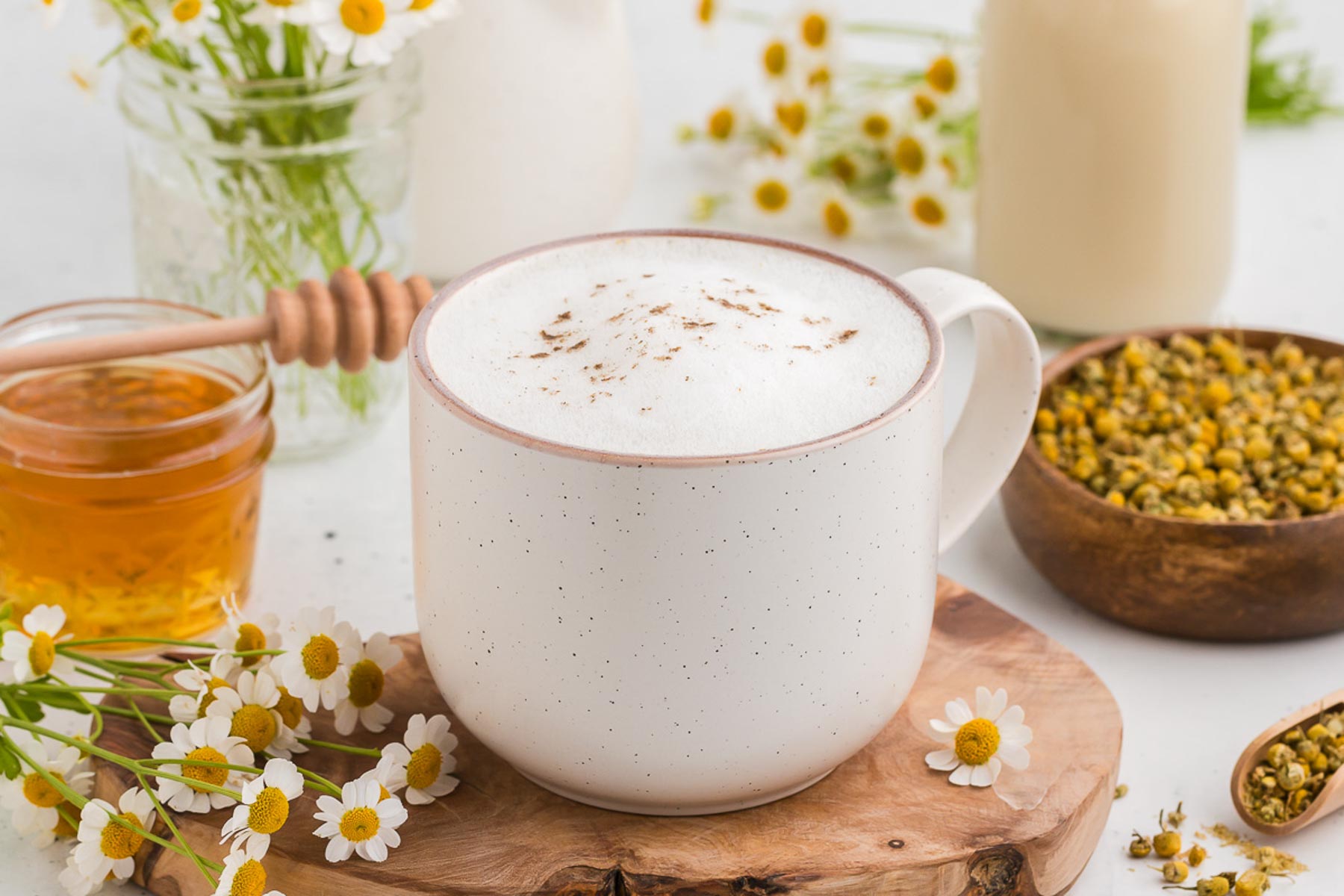 Chamomile latte on a wooden board with fresh and dried chamomile flowers in the background and a jar of honey