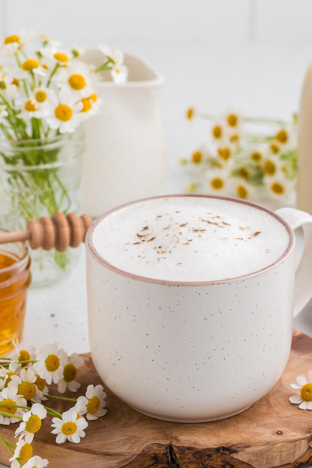 Stoneware mug full of Chamomile Latte on a wooden board and chamomile flowers in the background