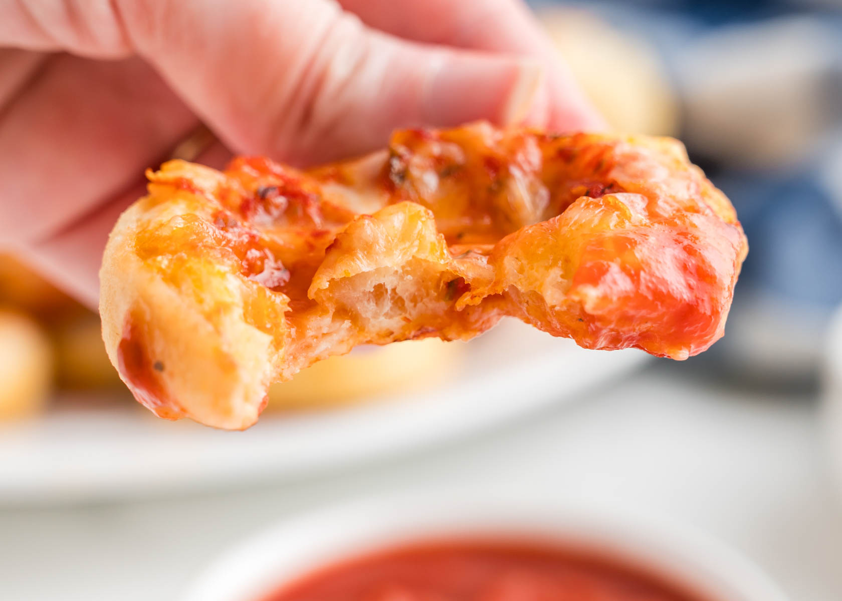 A person holding a pizza pinwheel with a bite out of it.
