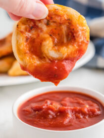 A hand holding a pizza pinwheel and dipping it into marinara sauce