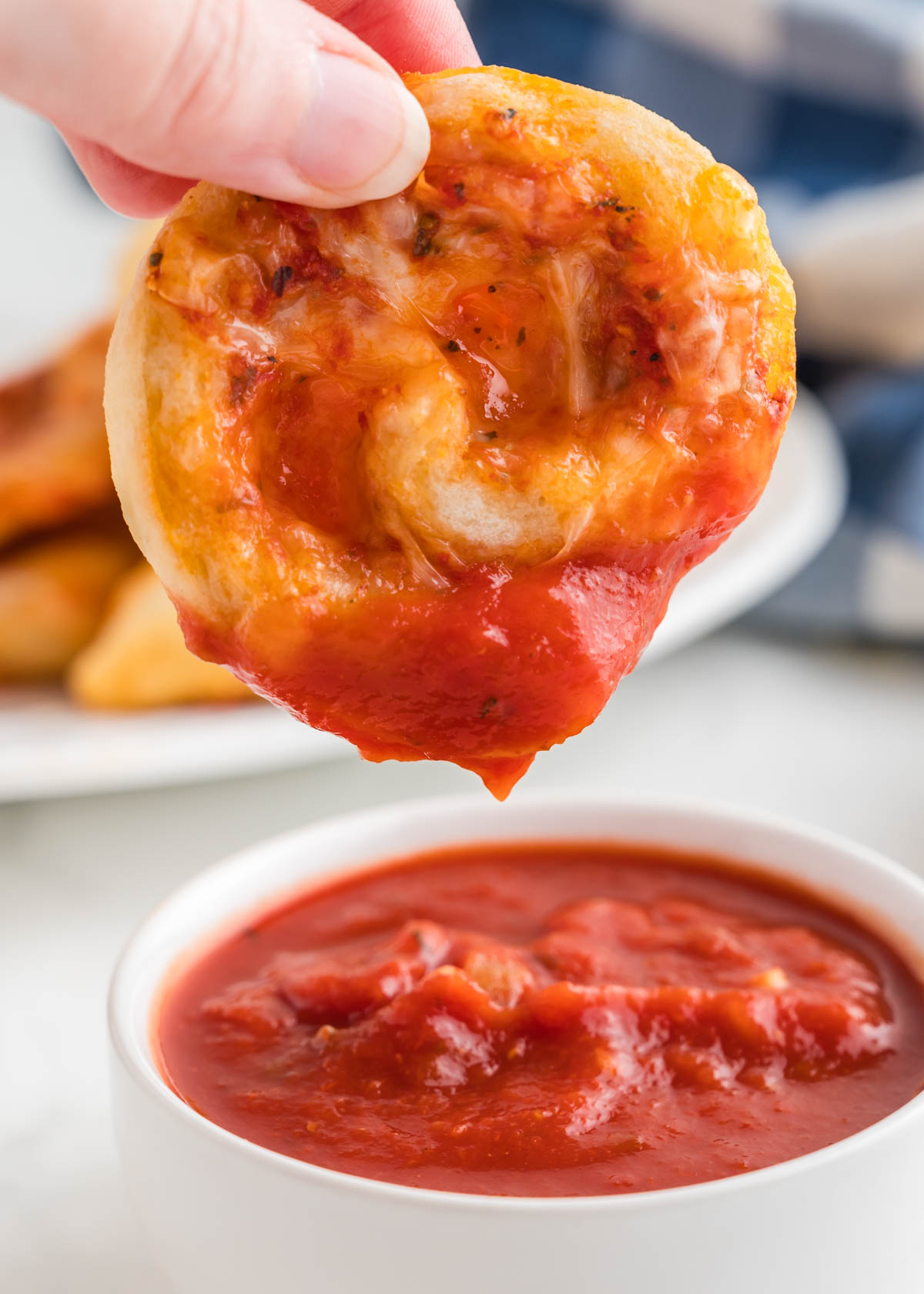 A hand holding a pizza pinwheel and dipping it into marinara sauce
