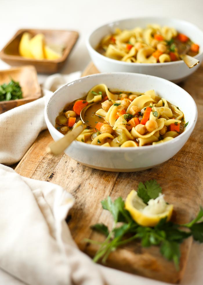 Two bowls of chickpea noodle soup on a wooden board. 