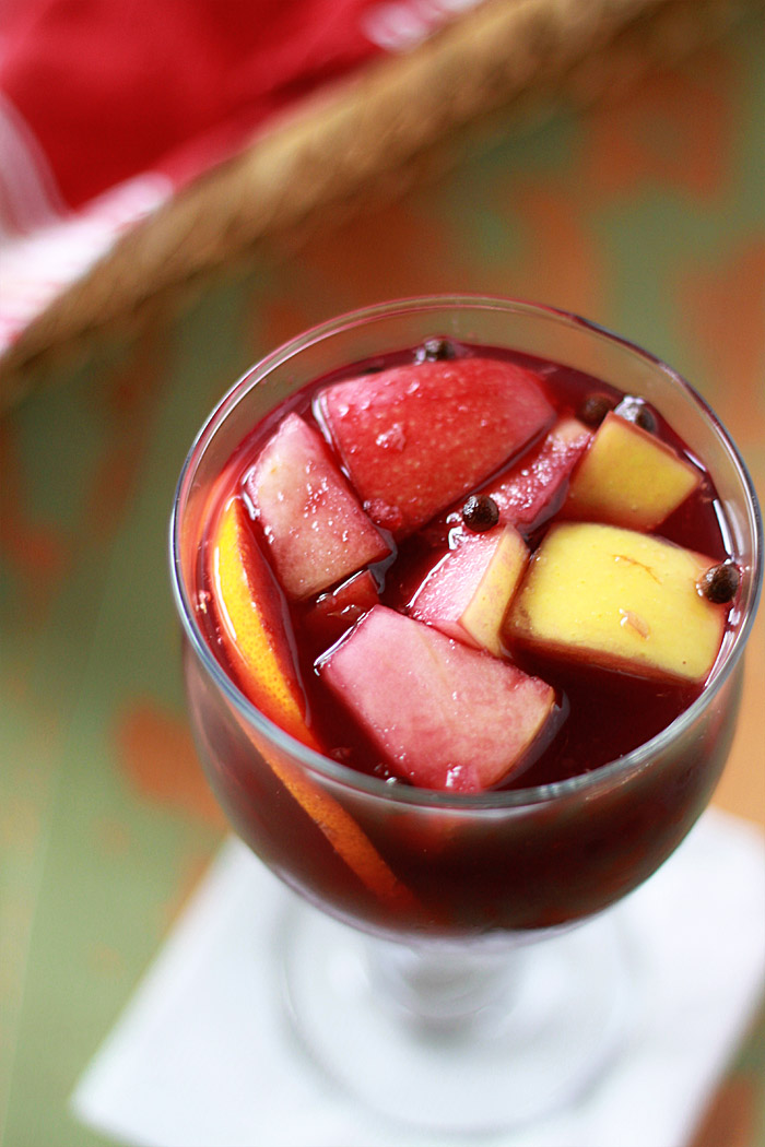 A close up of a glass full of red wine sangria against a green background.