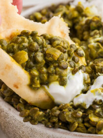 A hand scoops naan into Coconut Curried Green Lentils and yogurt.