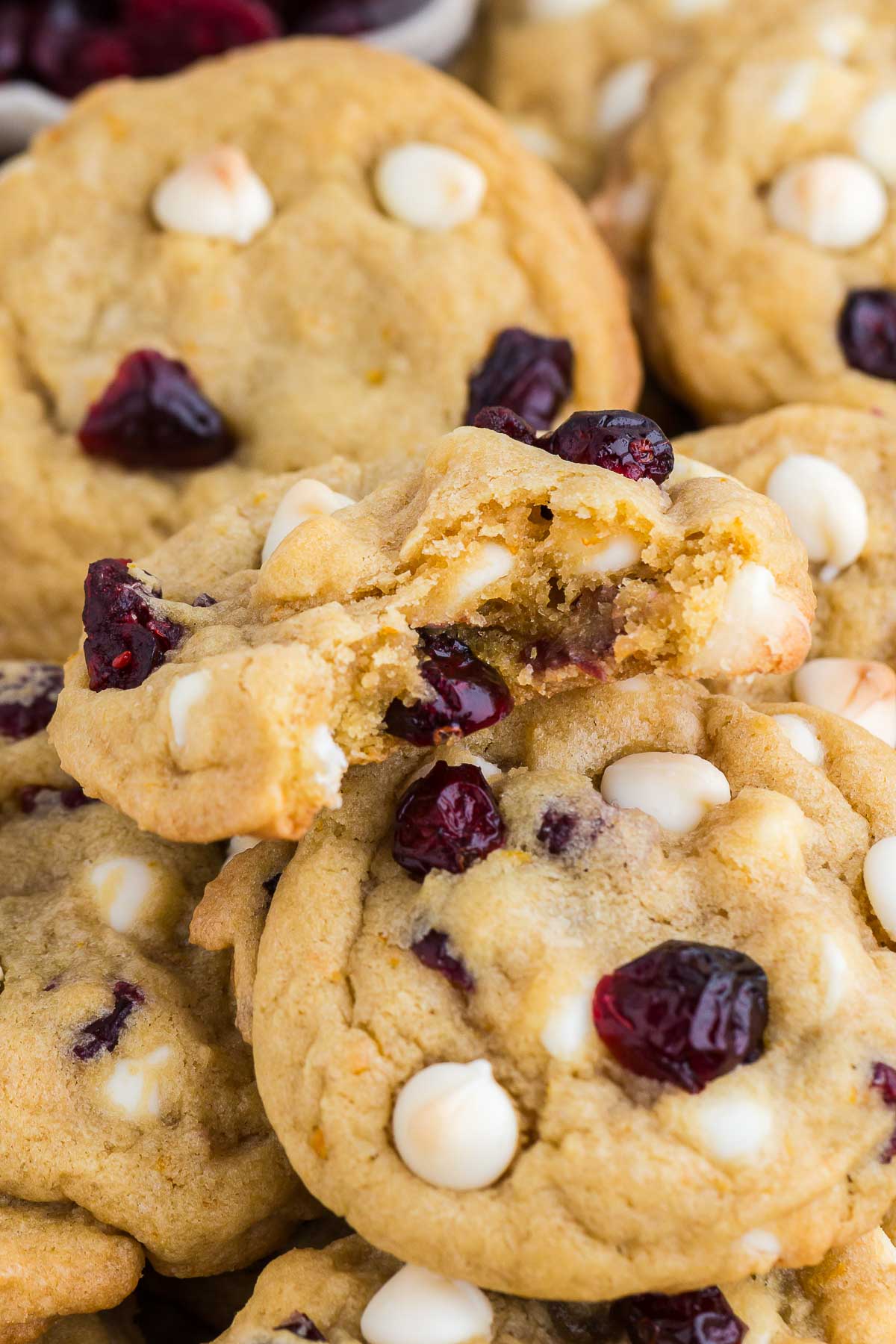 Close up of Cranberry Orange White Chocolate Chip Cookies, one with a bite out of it showing the soft and chewy interior