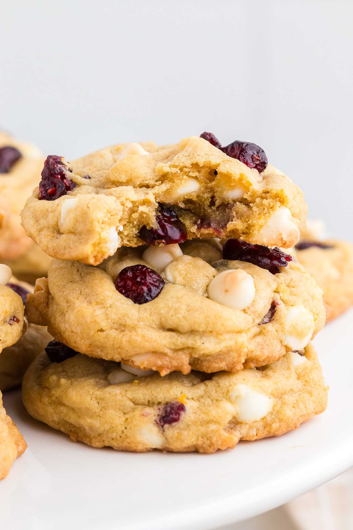 A stack of three Cranberry Orange White Chocolate Chip Cookies with a bite out of the top one. 