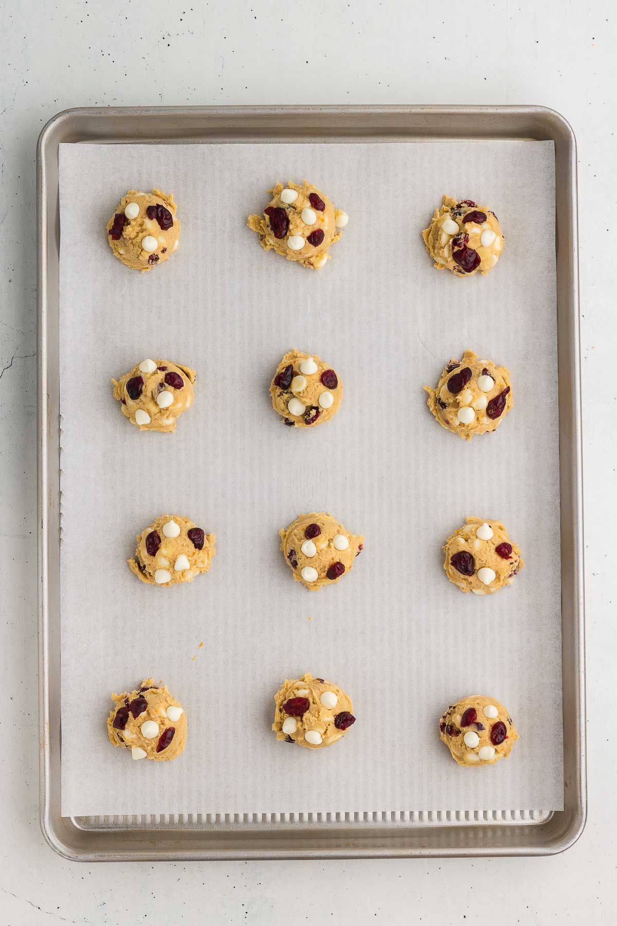 Cranberry Orange White Chocolate Chip Cookie dough balls dropped onto a parchment lined cookie sheet