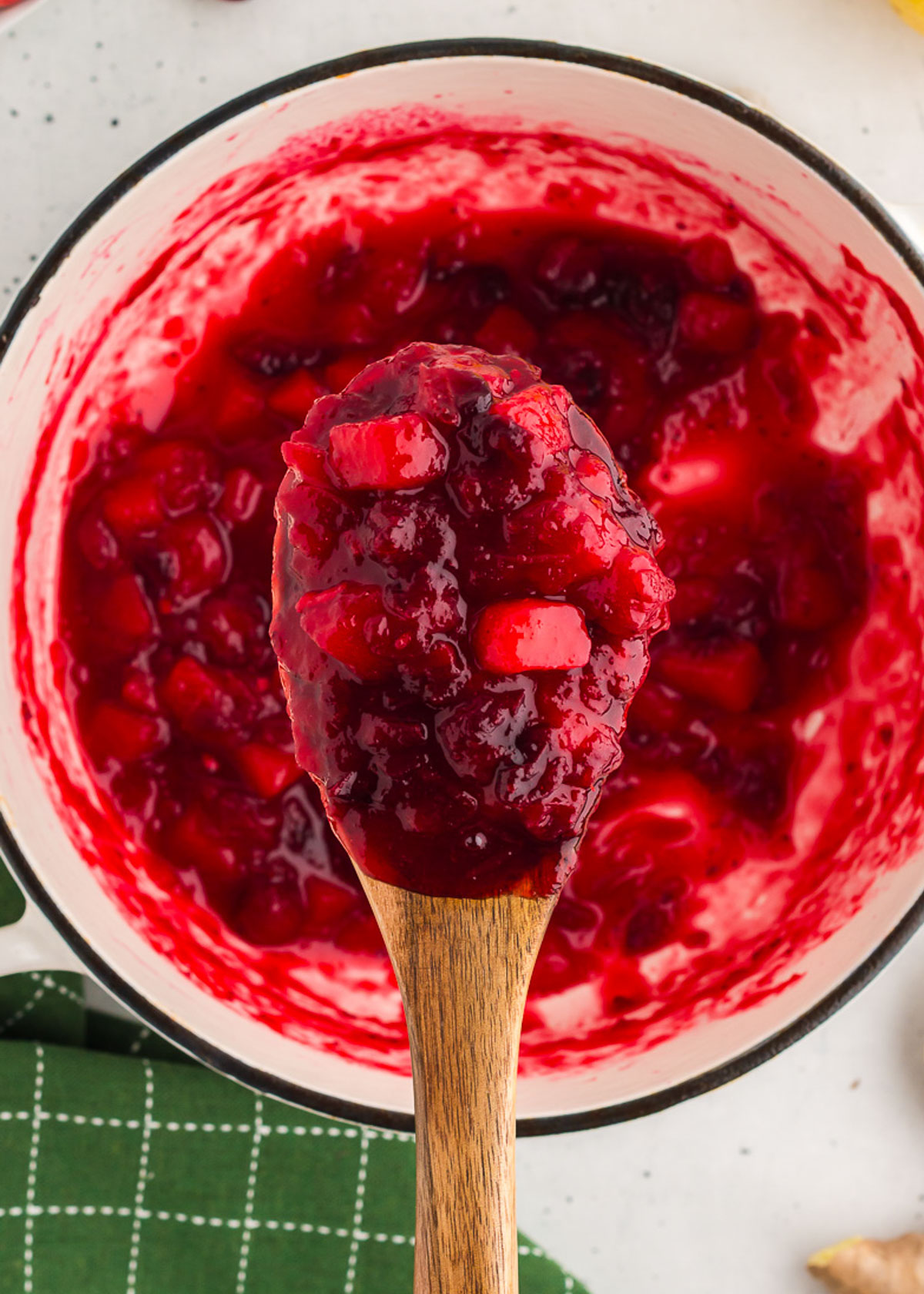 a wooden spoon holds ginger pear cranberry sauce up out of the saucepan