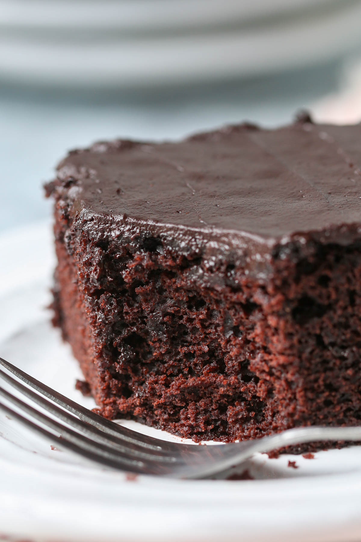A piece of chocolate wacky cake with a bite out of it on a white plate with a fork on it.