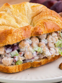 Creamy Chickpea Salad Sandwiches with Pecans & Grapes on a croissant on a white plate with grapes in the background