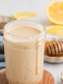 Creamy Lemon Tahini Dressing in a mason jar with a drip going down the side plus honey and lemon in the background