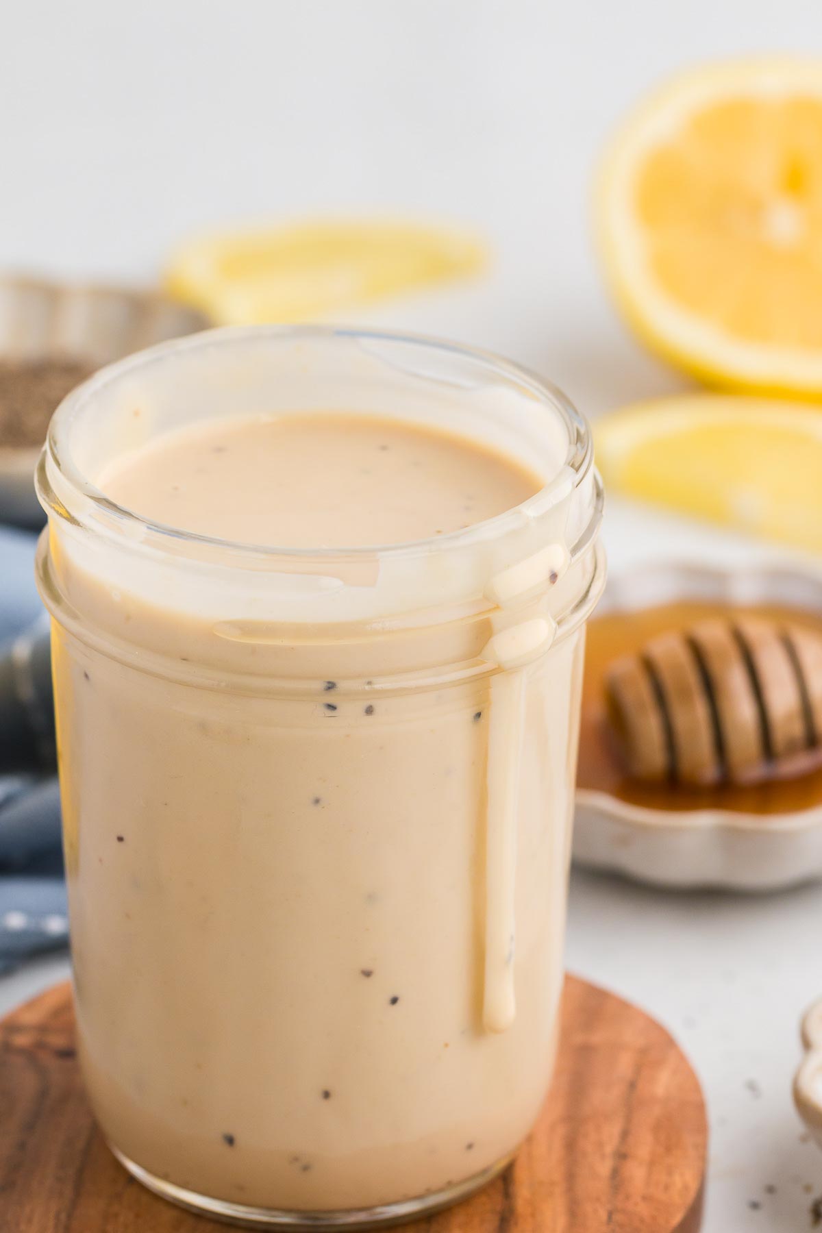 Creamy Lemon Tahini Dressing in a mason jar with a drip going down the side plus honey and lemon in the background