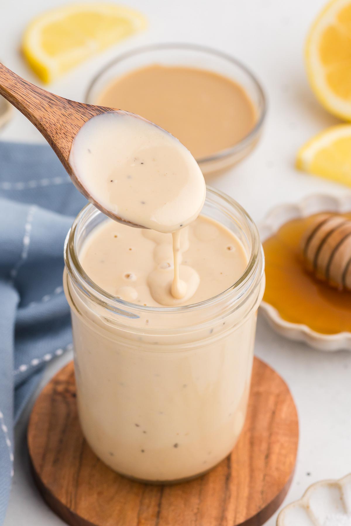 Dressing being drizzled by a spoon into a mason jar. The dressing is Creamy Lemon Tahini Dressing