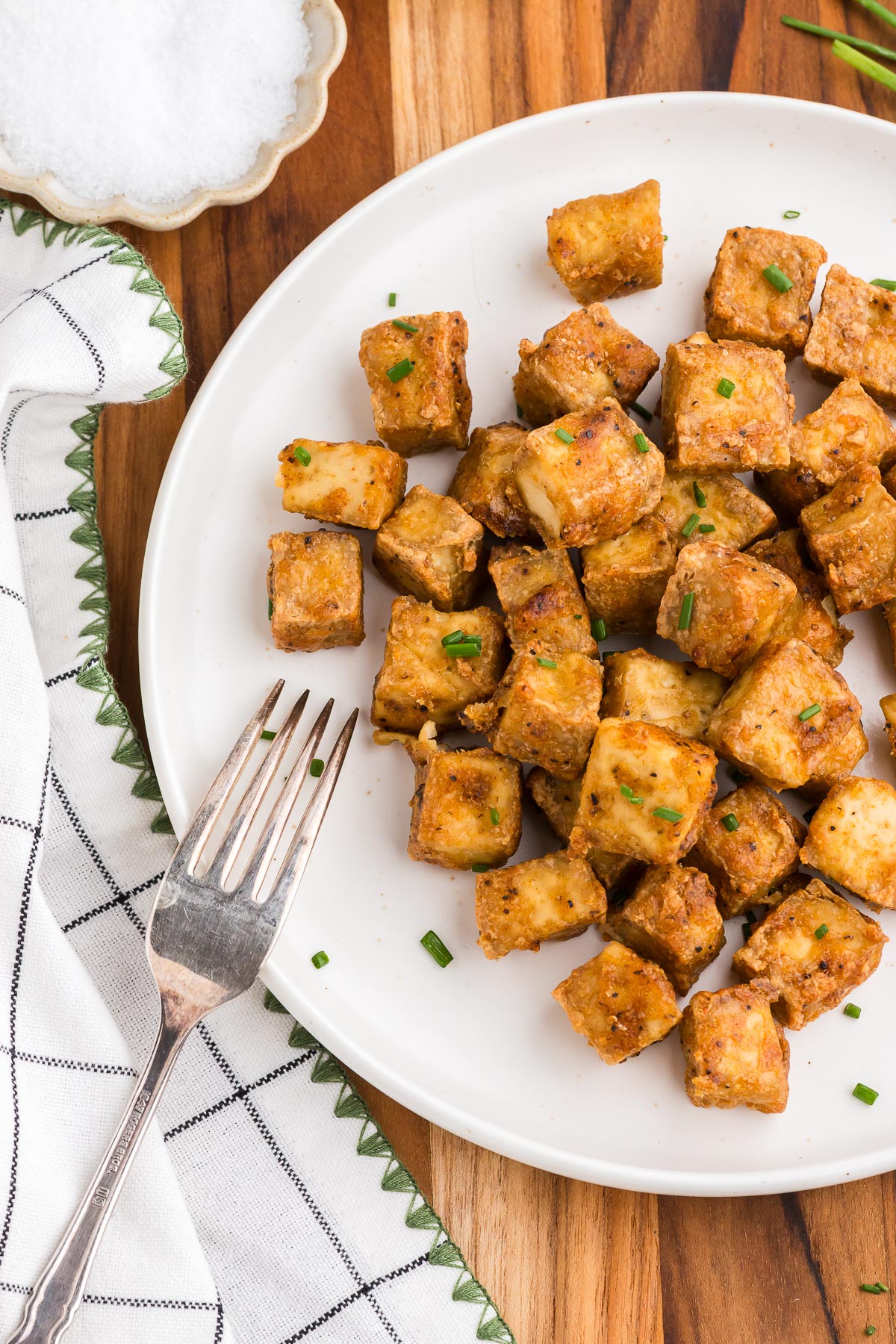 Top view of Crispy Air Fryer Tofu on a white plate with a silver fork and a windowpane plaid napkin