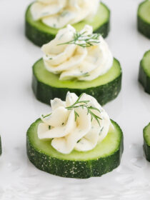 Cucumber cream cheese rounds with a sprig of dill on a white tray.