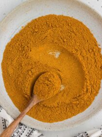 a bowl full of homemade curry powder mix with a wooden spoon