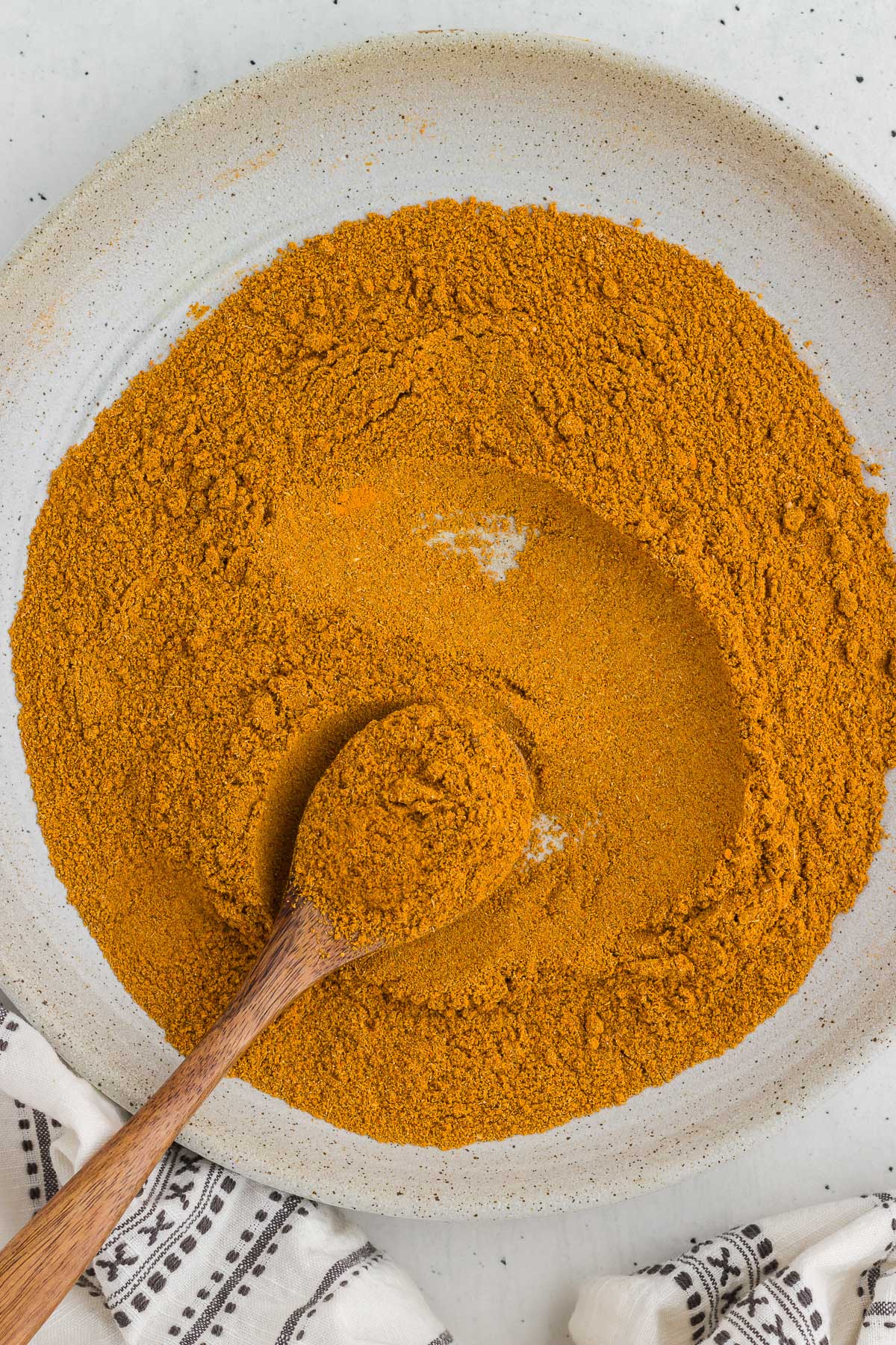 a bowl full of homemade curry powder mix with a wooden spoon