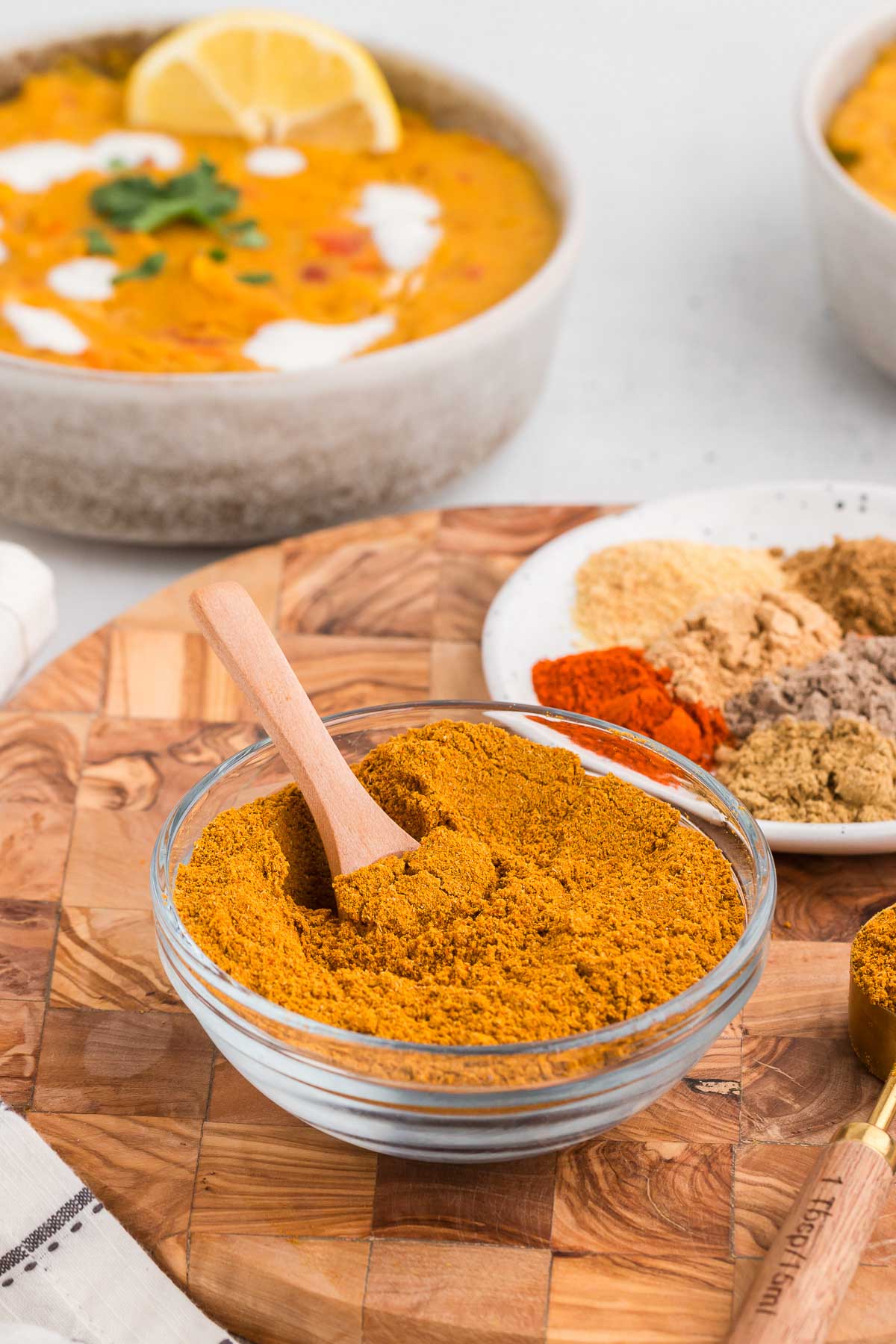 a glass bowl full of homemade curry powder mix with a wooden spoon