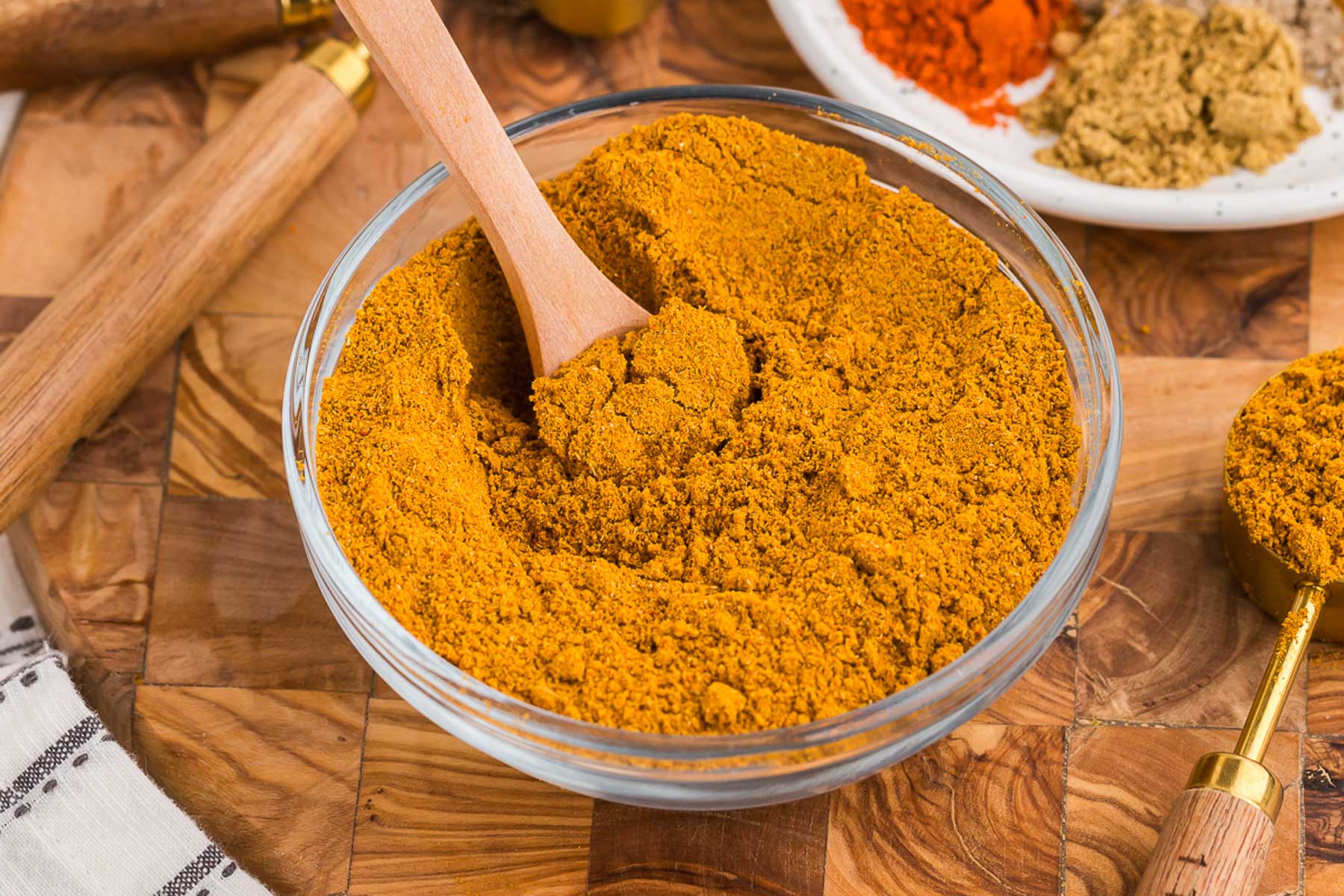 a glass bowl full of homemade curry powder mix with a wooden spoon