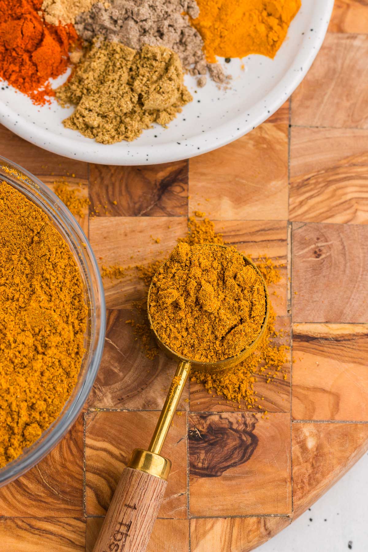 a gold scoop with homemade curry powder in it on a wooden board