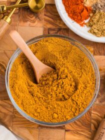 a glass bowl full of homemade curry powder mix with a wooden spoon