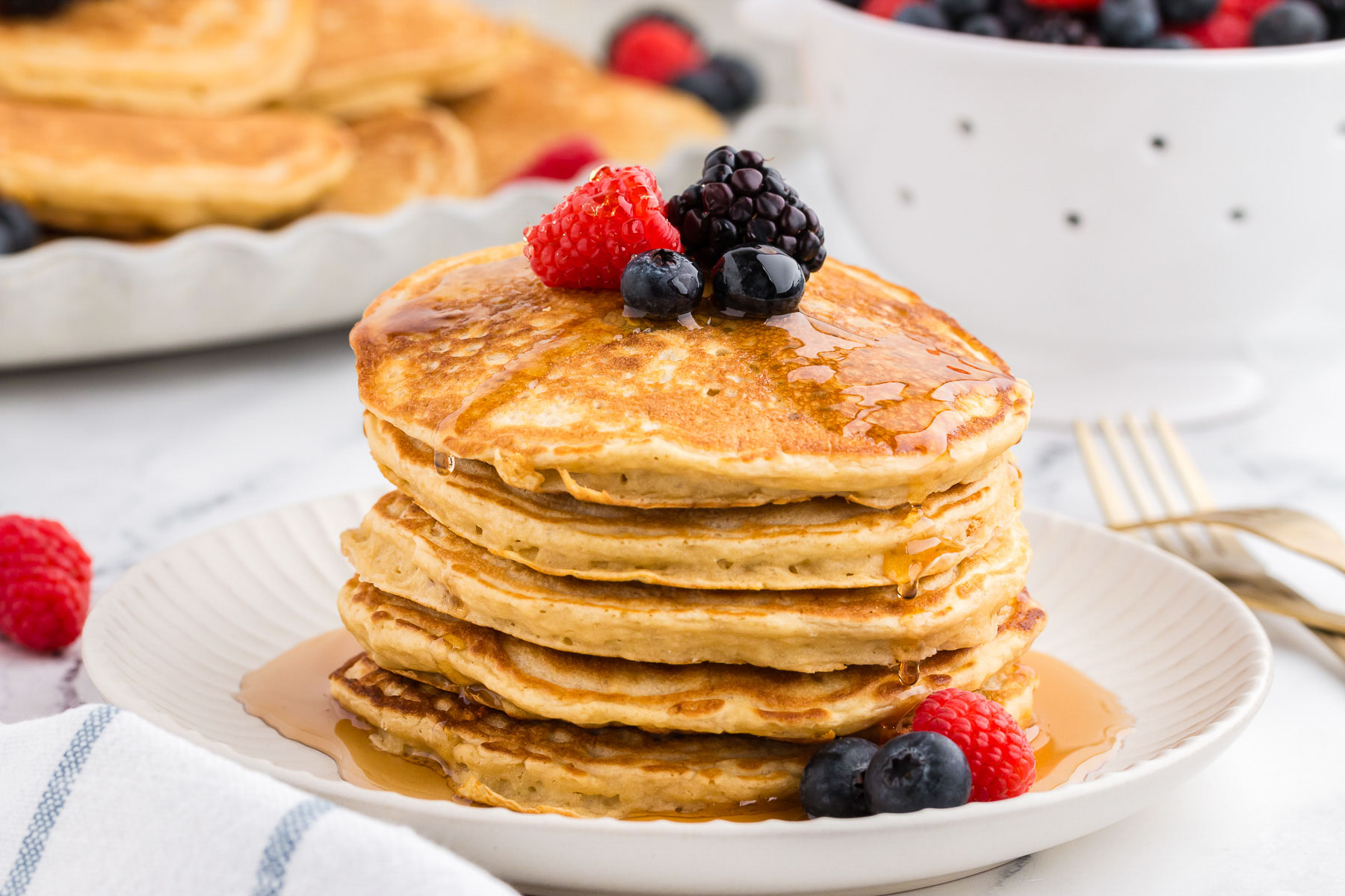 A plate of pancakes with thick maple syrup being drizzled on to the top. 