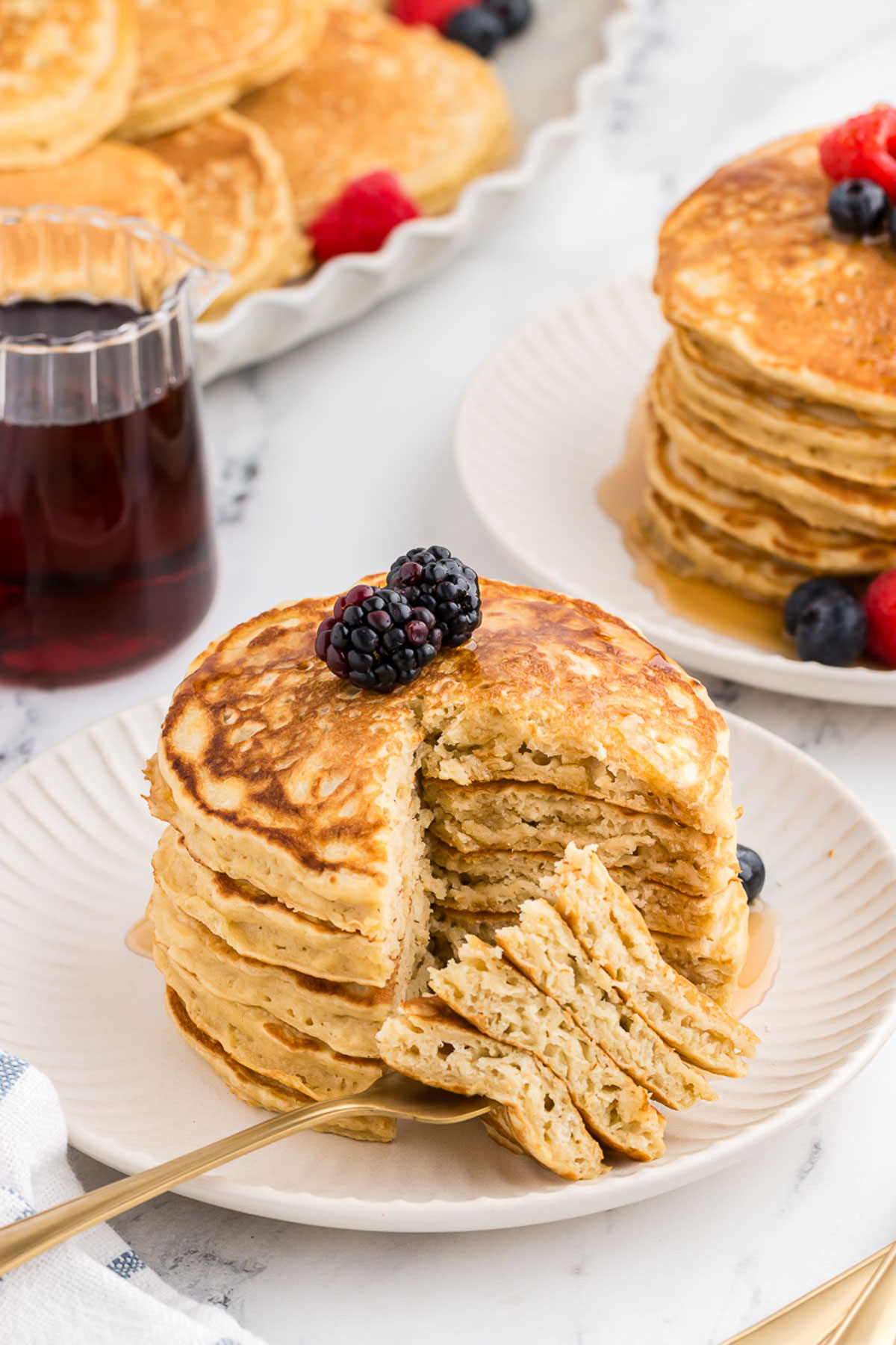 A top view of a platter full of dairy-free buttermilk pancakes with berries in the background